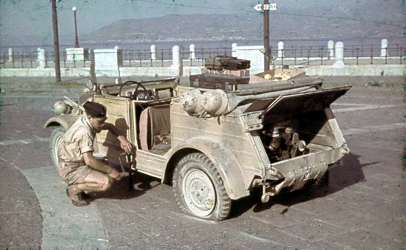 Italy, Sicily, 1943. A flat tire on a VW-Kübelwagen, soldier with jack going to replace the tire. Note the open engine compartment. - By Bundesarchiv CC BY-SA 3.0