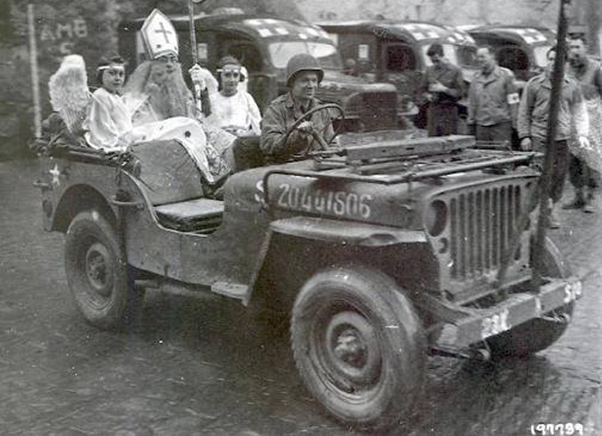 US Army 28th Infantry Division soldier CPL Dick Brookins (22 at the time) plays St. Nicholas for the children of Wiltz, Luxembourg, Christmas season 1944. Wiltz had four years of German occupation without their traditional Christmas parade and visit from St. Nick. Another American soldier, Harry Stuts, suggested and organized the celebration, a symbol of the town's liberation from the Germans. WC-54 3/4-ton Ambulances in background. Photo source: Pinterest