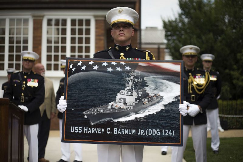 A Marine holds a poster of the future Arleigh Burke-class guided-missile destroyer USS Harvey C. Barnum, Jr. (DDG-124) during a ceremony July 28, 2016 at the Marine Barracks in Washington, D.C.  Source: Wikipedia/ Public Domain