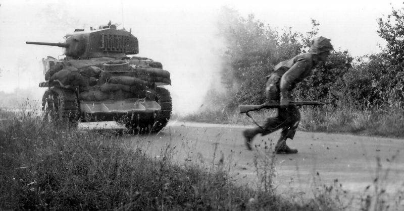 American Soldier crosses the road, covered by an M5A1 stuart tank, note the hedgerow clipping device on the front of the tank.