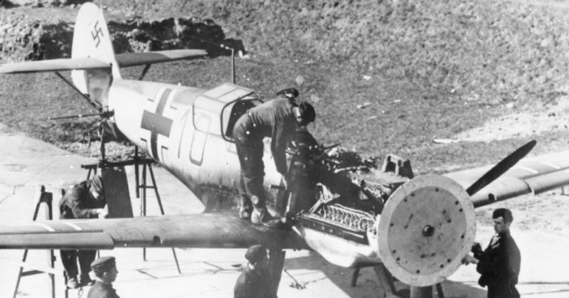 The synchronization gear of a Messerschmitt Bf 109E is adjusted, 1941. A wooden disk attached to the propeller is used to indicate where each round passes through the propeller arc. Bundesarchiv - CC BY-SA 3.0
