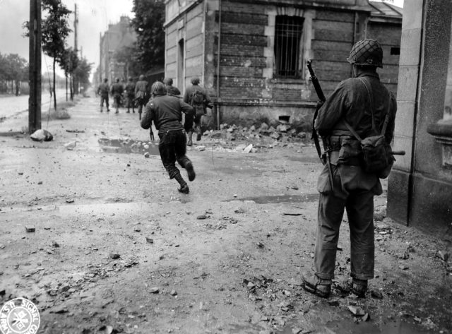 American troops advance forward as they clear the streets of Cherbourg. Image Source: Wikimedia Commons/public domain.