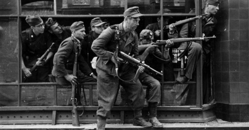 Members of the SS-Sonderregiment Dirlewanger in a window of a townhouse at 9 Focha Street in Warsaw, August 1944. In the glass reflection one can identify details of the tenement on the opposite side of the street. <a href=