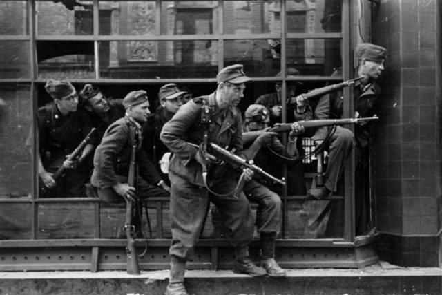 Members of the SS-Sonderregiment Dirlewanger in a window of a townhouse at 9 Focha Street in Warsaw, August 1944. In the glass reflection one can identify details of the tenement on the opposite side of the street. Photo Credit.