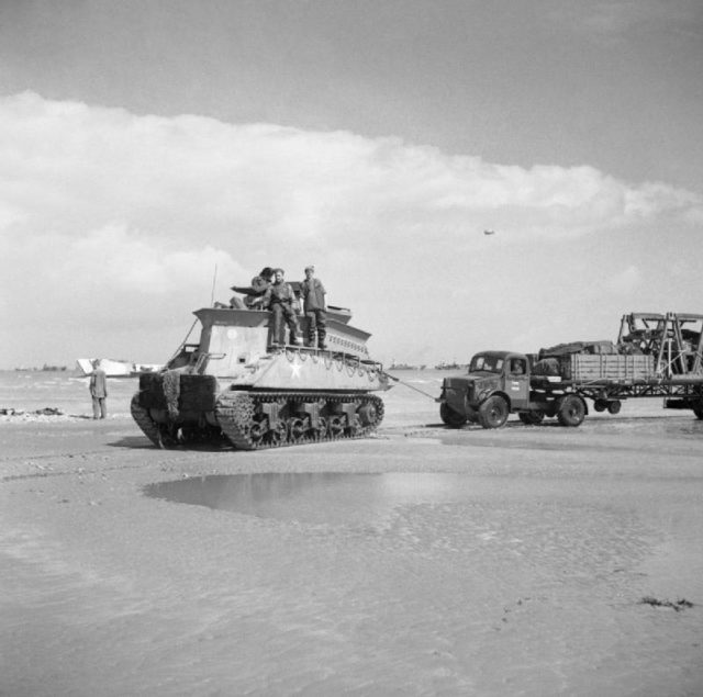 A Sherman BARV tows a disabled Bedford articulated lorry and trailer off the beach. Photo Credit.