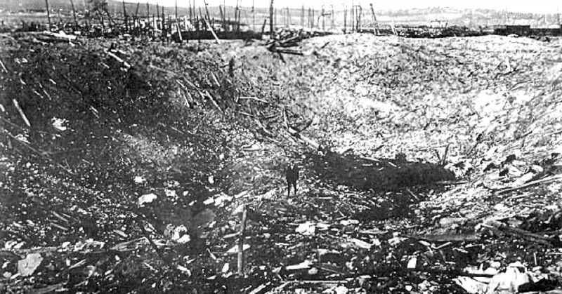 A person stands in the huge crater caused by the explosion.  