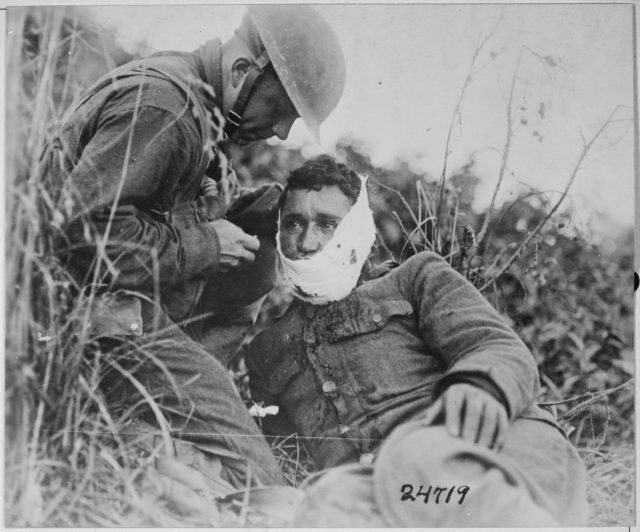 Soldier of Company K, 110th Regiment Infantry receiving first-aid treatment from a comrade. Varennes-en-Argonne, France, 1918.