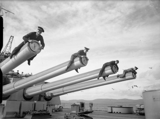 Royal Marines straddling the barrels whilst they fit the tampions to the 14-inch guns of HMS HOWE.