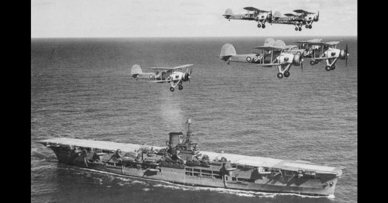 The aircraft carrier HMS Ark Royal with a flight of Swordfish overhead, 1939.