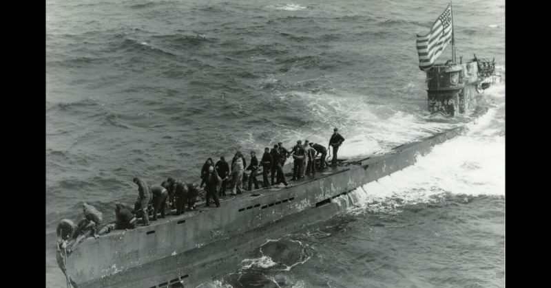 A boarding party from the USS Pillsbury (DE 133) works to secure a tow line to the newly captured German U-boat U-505 on Jun 4, 1944. Note the large U.S. flag flying from the periscope. 