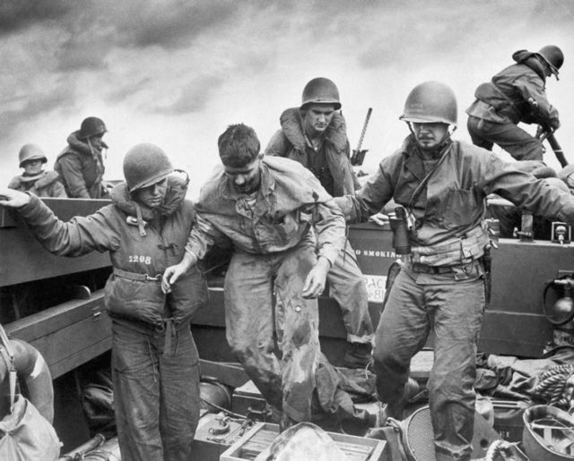 US Coast Guardsmen assisting a wounded Marine into an LCVP after the Marine’s LVT sustained a direct hit while heading to the landing beaches on Iwo Jima, February 1945.