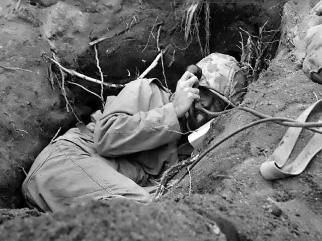 Burrowed in his shallow foxhole at the edge of Motoyama airstrip on Iwo Jima, an US Marine communicator called for artillery support, February 1945.