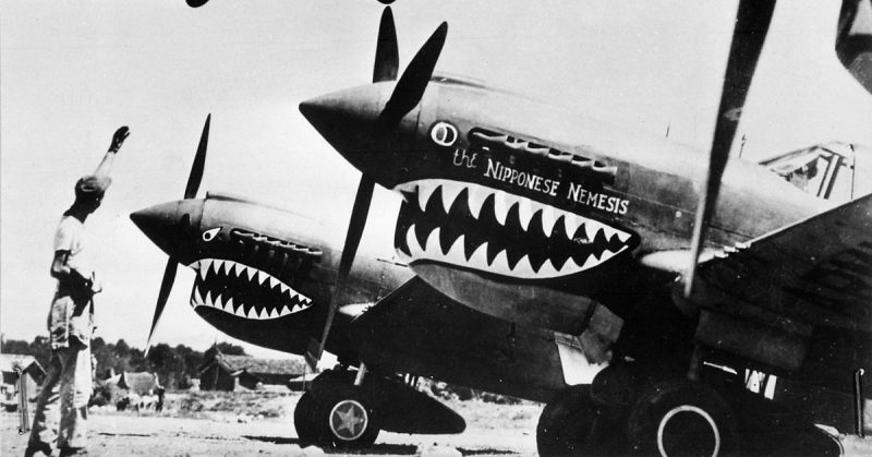 Liberator bomber crosses the P-40 fighter planes at an advanced U.S. base in China. An American soldier waves good luck to the crew, off to bomb Japan.