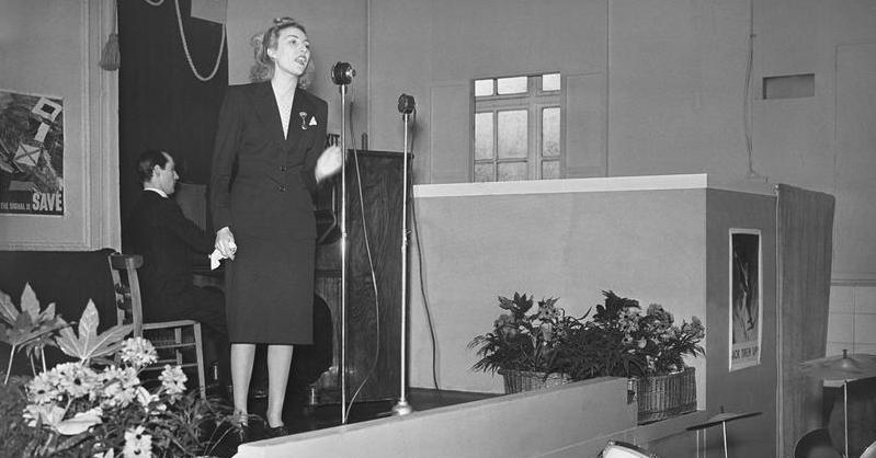 The singer Vera Lynn, who became so popular with British servicemen that she was known as the 'Forces' Sweetheart' sings to workers during their lunch break at a factory in the south of England. <a href=http://www.iwm.org.uk/collections/item/object/205195973>Photo Credit</a>