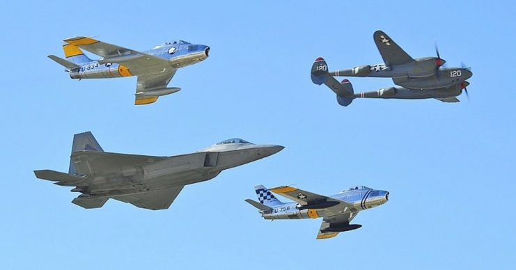 US-built aircraft fighters representing different eras; a World War II P-38 Lightning, a pair of F-86 Sabres from early jet age and a modern F-22 Raptor.