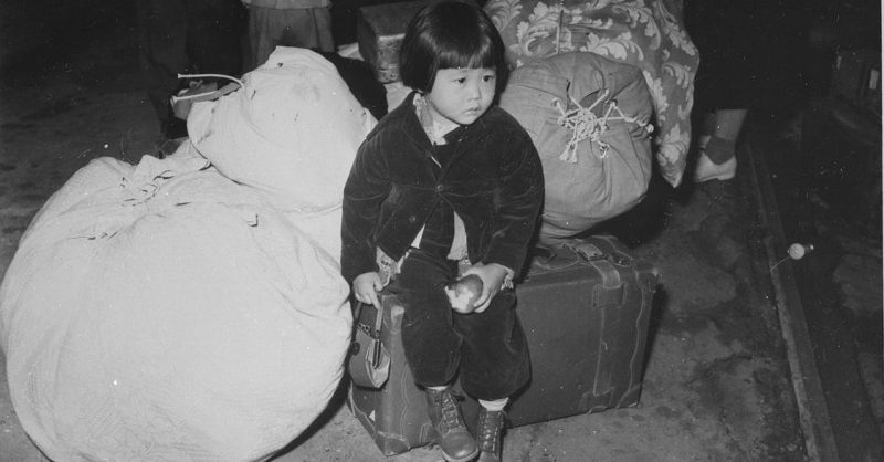 A young evacuee of japanese ancestry waits with the family baggage before leaving by bus for an assembly center. 