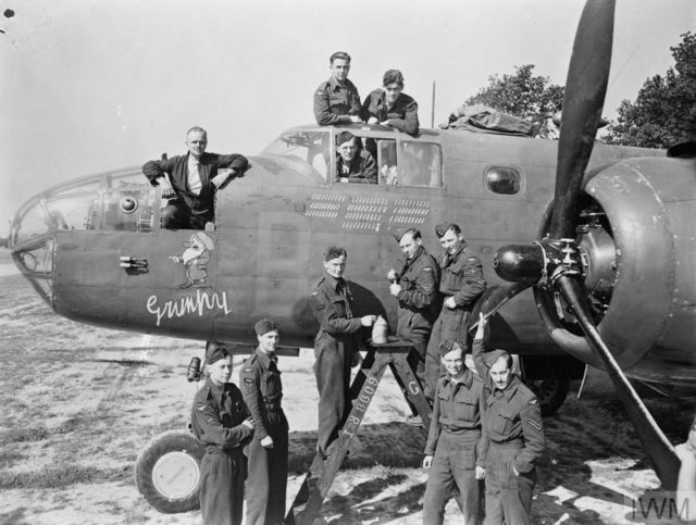 Ground personnel of No. 98 Squadron RAF, who serviced North American Mitchell Mark III, HD372 ‘VO-B’ “Grumpy”, during its record operational career, gather at the aircraft’s nose at Dunsfold, Surrey, as Corporal V Feast paints the 102nd bomb symbol onto its tally of operations.
