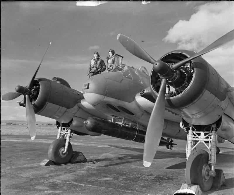 The crew of a Bristol Beaufighter Mark VIC (ITF) of No 144 Squadron RAF stand by the cockpit of their aircraft at a dispersal at Tain, Ross-shire. The Interim Torpedo Fighter, or "Torbeau" as this version was known, is armed with a Mark XII aerial torpedo. Note the aerial camera port in the nose.