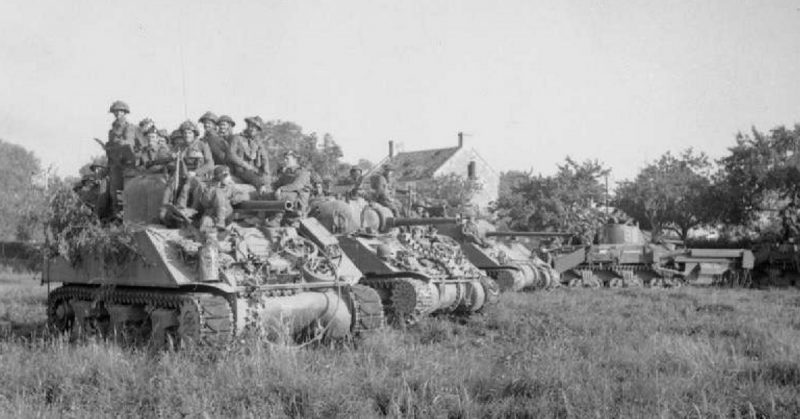 Two M4 Sherman tanks and a Sherman Firefly carrying infantry and a Sherman Crab wait for the order to advance at the start of Operation Goodwood, 18 July.