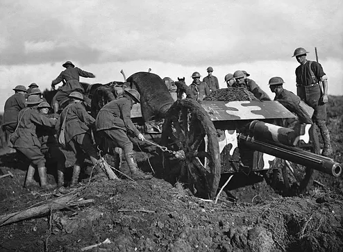 An 18 pounder gun being hauled through the mud at Broodseinde Ridge to a position further forward, in support of the advancing Australians, two days before the initial attack on Passchendaele Ridge, in the Ypres sector. Identified, left of the gun, left to right: Gunner (Gnr) W E Drummond Gnr J Brannon (to Drummond’s right) Gnr C V Cox (in front of Brannon) two men unidentified behind Cox 34401 Gnr A Hewitt (in front of Cox) Dvr A C Sampson (standing on wheel, back to camera) Gnr G G Dowling (foreground, pulling rope on front wheel) Right side of gun, left to right: Dvr Hughes Dvr F Peace unidentified unidentified Bombardier T (R ?) Garniss Sergeant W Reynolds (extreme right, standing back).