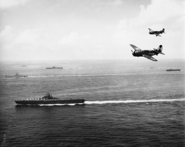 SB2C Helldivers flying over USS Essex during the Okinawa campaign, May 1945. USS Bunker Hill, USS Langley, and other vessels in background.