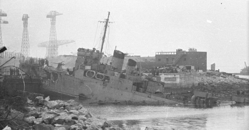 Left: The Normandie Dock months after the raid. The wreck of HMS Campbeltown can be seen inside the dry dock. Right: HMS Campbeltown wedged in the dock gates. Note the exposed forward gun position on Campbeltown and the German anti-aircraft gun position on the roof of the building at the rear. Bundesarchiv - CC BY-SA 3.0 de