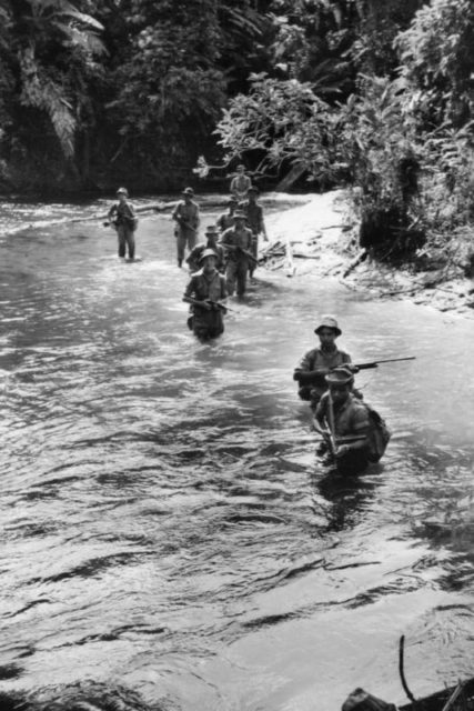 Men of the Malay Police Field Force wade along a river during a jungle patrol in the Temenggor area of northern Malaya.