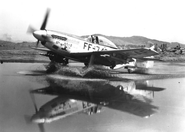 F-51 Mustang, laden with bombs and rockets, taxis through a puddle at an airbase in Korea.