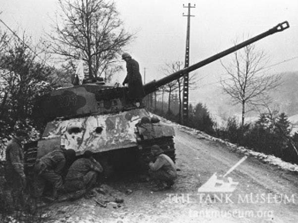 An abandoned Tiger II, with white flag flying, being inspected by American troops, in the Ardennes, France 1945.