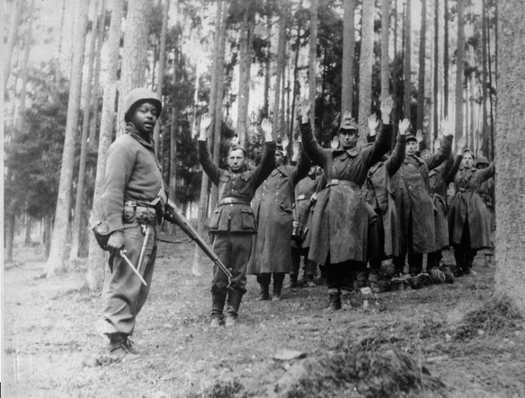 This soldier of the 12th Armored Division is standing guard over a group of German prisoners in April 1945. 