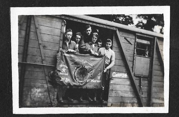 A photograph of the marine of Marines from the 96th Co (H). 6th Marine Regiment as they prepare to leave the 3rd U.S. Army Railhead at Koblenz, Germany.The Marines are holding a locally made German “Unit Banner” of the 2nd Battalion, 6th Marine Regiment. Photo credits: James Gregory