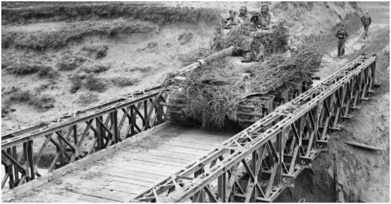 A heavily camouflaged Sherman tank crosses a Bailey bridge over the River Santerno near Imola.