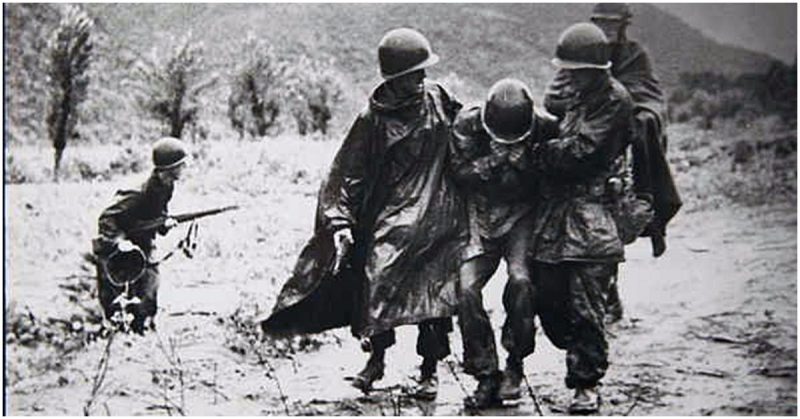 Capt. Emil Kapaun (right), former chaplain with Headquarters Company, 8th Cavalry Regiment, 1st Cavalry Division, helps another soldier carry an exhausted Soldier off the battlefield early in the Korean War.