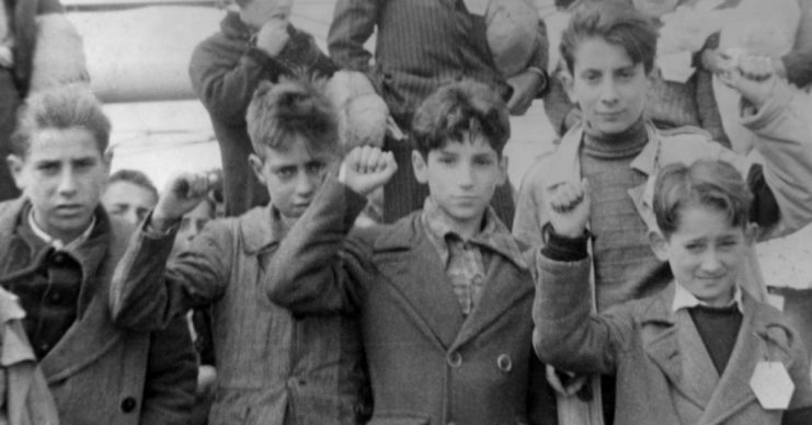 Children preparing for evacuation, some giving the Republican salute. The Republicans showed a raised fist whereas the Nationalists gave the Roman salute.