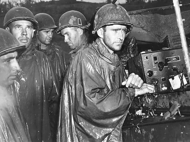 May 8, 1945: Miserable-looking soldiers listen in the rain to the announcement of victory in Europe from the Island of Okinawa. For these brave men, the horrors of war were far from over.