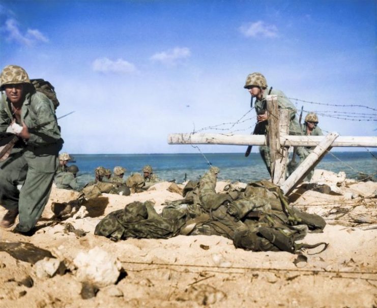 A group of fighters, led by a Marine with a wounded hand, charging from the shore around opened barbed-wire entanglement to battle firmly entrenched Japanese in pillboxes on Tarawa. The leader is carrying his bayoneted rifle in the crook of his arm instead of with his wounded hand. Royston Leonard / mediadrumworld.com