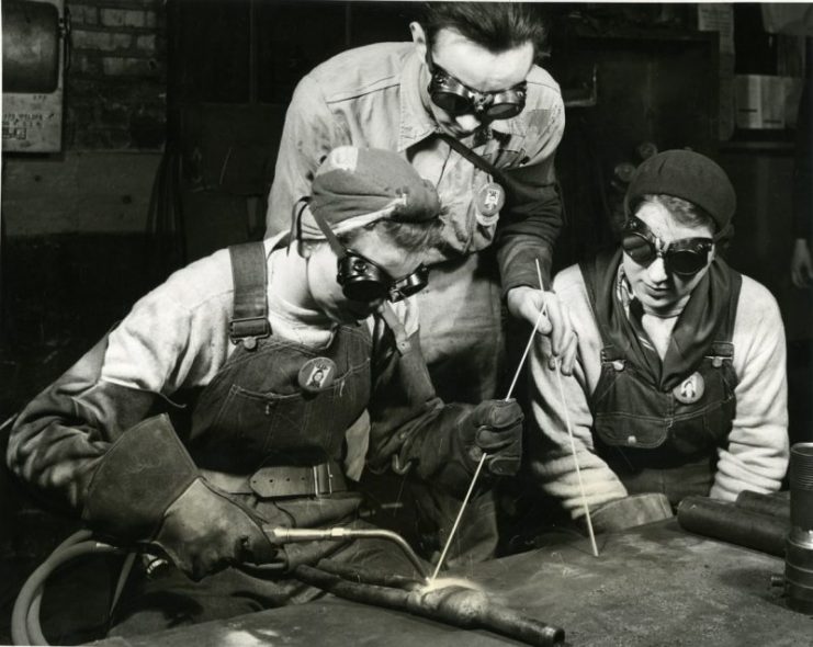 Peggy Bridgeman at the left demonstrates to Ruth Harris the correct technique while their instructor, Lee Fiscus, looks on attentively, in the Gary plant of the Tubular Alloy Steel Corporation, United States Steel Corporation subsidiary. Peggy is acclaimed by her superiors to be one of the most skilled welders they have had working with them.