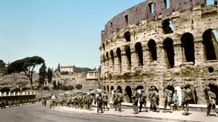 United States troops walk down a curved street past the Coliseum in Rome, Italy. A Roman gentleman walks in the opposite direction, using a cane. The troops carry their packs and weapons. Italy surrendered to the Allies on September 8, 1943. Paul Reynolds / mediadrumworld.com