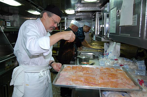 Chef Tenney Flynn, co-owner of the New Orleans seafood restaurant GW Fins, seasons a tray of fish fillets in the galley of the ballistic missile submarine USS Louisiana (SSBN 743). Flynn helped Louisiana’s culinary specialists prepare some of GW Fins’ popular dishes for lunch while he was visiting. (U.S. Navy photo by Lt. Ed Early/Released)