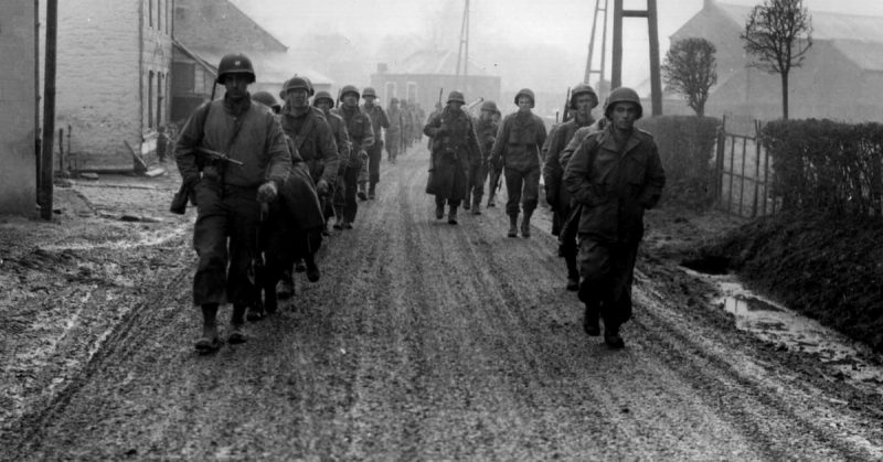 Men of the 28th Infantry Division march down a street in Bastogne, Belgium, December 1944. Some of these men lost their weapons during the German advance in this area.