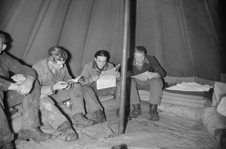 A group of German Prisoners of War read as they sit around the inside edge of a bell tent at a PoW camp, somewhere in Britain, 1945.