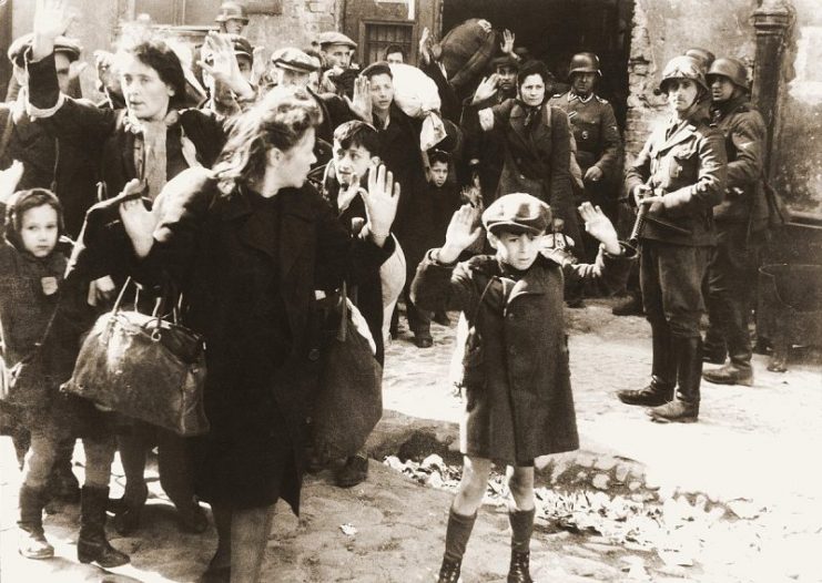 Originally captioned “Forcibly pulled out of dug-outs,” this Stroop Report photo shows SS man Josef Blösche pointing his gun at people during the Warsaw Ghetto Uprising