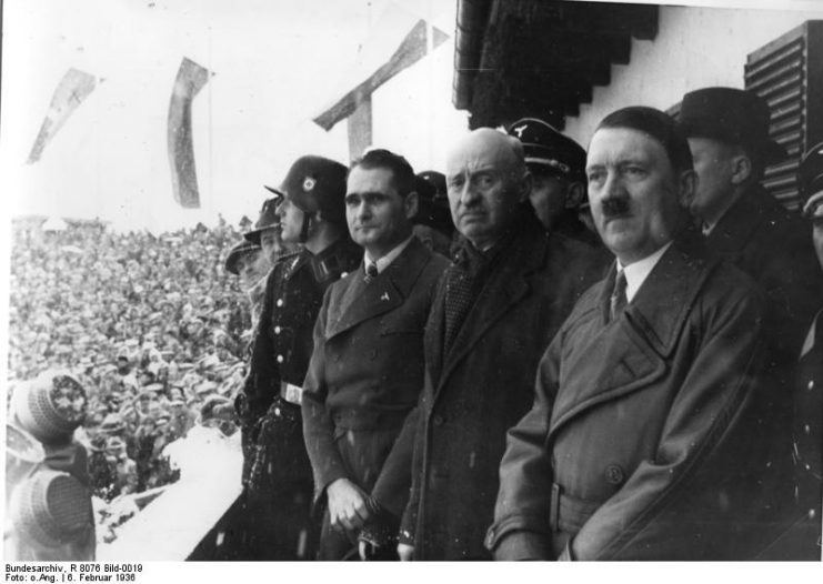 Opening Ceremony with Rudolf Hess, president of IOC count Henri de Baillet-Latour, and Adolf Hitler. By Bundesarchiv – CC BY-SA 3.0 de
