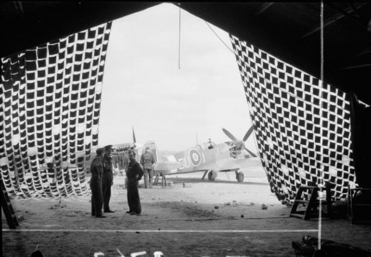 Supermarine Spitfire LF Mark IXBs of Nos. 312 and 313 (Czech) Squadrons RAF undergoing engine repair and maintenance at Appledram, Sussex, viewed through the entrance of a Butler combat hangar covered with camouflage netting.
