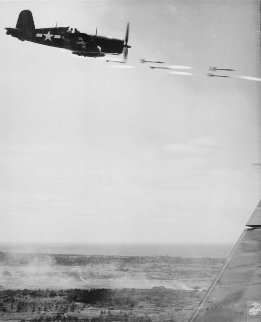 Corsair fighter looses its load of rocket projectiles on a run against a Japanese stronghold on Okinawa. In the lower background is the smoke of battle as Marine units move in to follow up with a Sunday punch