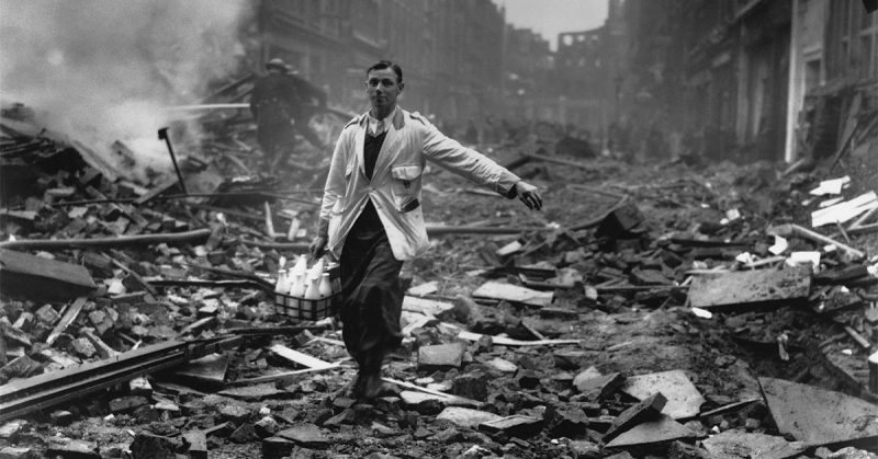A milkman delivering milk in a London street devastated during a German bombing raid. Firemen are dampening down the ruins behind him. (Photo by Fred Morley/Getty Images)