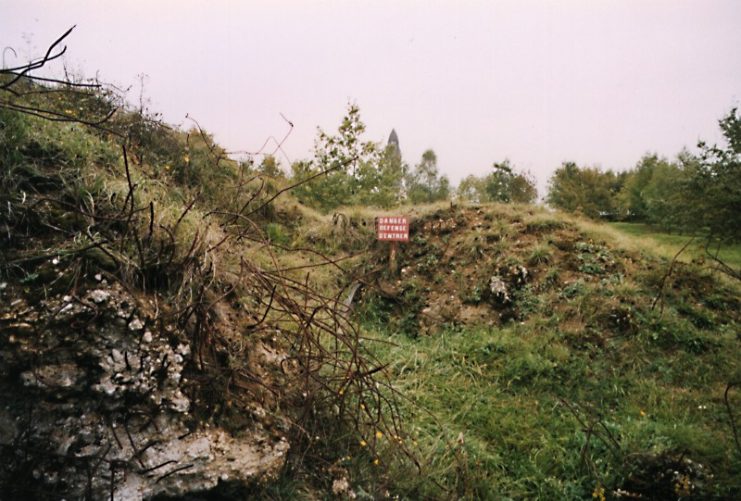 Former battlefield at Fort Thiaumont, in the background of the tip of Douaumont ossuary. The inscription on the plate reads: DANGER DEFENSE D’ENTRER (Danger, Access Forbidden). Photo: Schreibkraft / CC-BY-SA 3.0