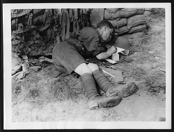 Soldier writing on a small piece of paper, possibly a letter home, Belgium 1917.