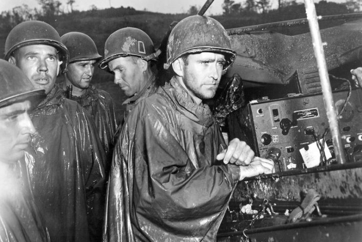 Soldiers in the U.S. Army’s 77th Infantry Division listen intently to the news of Germany’s surrender on May 8, 1945, thereafter known as Victory in Europe Day. Despite the good news, their faces remain battle-hardened, as they stand several yards behind the frontlines of continued fighting in Okinawa, Japan. Just minutes after the photograph was taken, the men were back at their posts. (Photo: “Army in Okinawa on VE Day,” cropped, CC BY-NC-SA 2.0 by England via Flickr)
