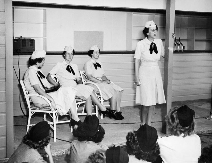 An unidentified U.S. Navy WAVES lieutenant speaks to fellow WAVES during a talk at NAS Barbers Point, Territory of Hawaii. Seated at far right behind her is CAPT Mildred McAfee, the first to hold the post of Director, WAVES.